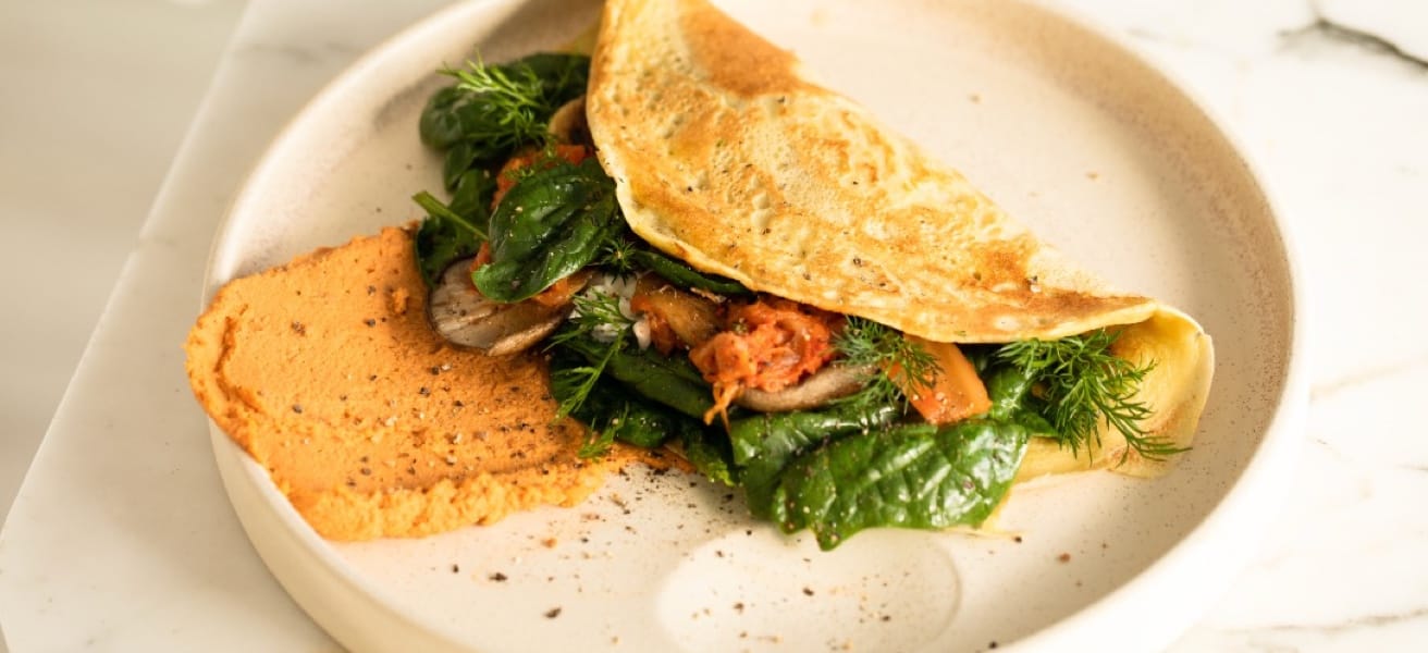 an image of an omelette filled with vegetables, spinach, and meat